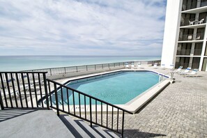 Una piscina con vista al océano, sillas de descanso y un edificio con balcones.