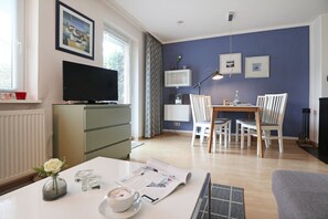 Ein modernes Wohnzimmer mit einem Flachbildfernseher, einem Essbereich mit Tisch und Stühlen sowie einer blauen Akzentwand.