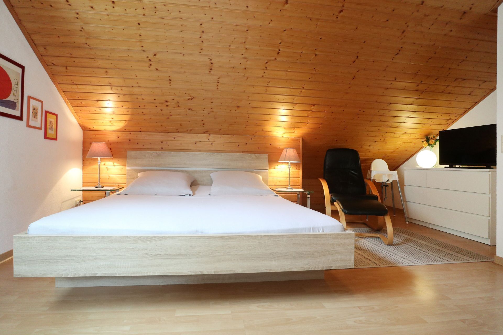 A bedroom with a large bed, two bedside lamps, a chair, a TV, and a dresser.