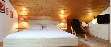 A bedroom with a large bed, two bedside lamps, a chair, a TV, and a dresser.