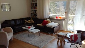 A living room with a black sofa, a white coffee table, a red and white chair, and a bookshelf. - Ferienwohnung Hammermühle - Aktivurlaub im Herzen der Oberpfalz (Freudenberg)
