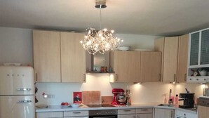 A modern kitchen with wooden cabinets, a dining table with chairs, a chandelier, and a refrigerator. - Ferienwohnung Hammermühle - Aktivurlaub im Herzen der Oberpfalz (Freudenberg)