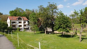 A two-story house with a balcony, surrounded by a grassy area and trees. - Ferienwohnung Hammermühle - Aktivurlaub im Herzen der Oberpfalz (Freudenberg)