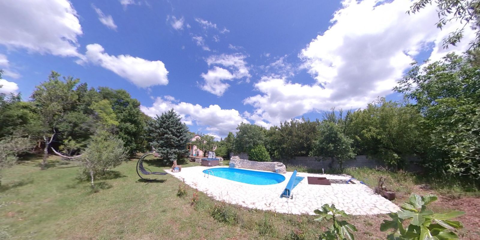 A backyard with a swimming pool, surrounded by trees and a grassy area.