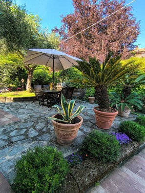 A patio with stone flooring, a table with chairs, a large umbrella, and potted plants.
