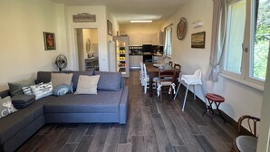 A modern living room with a grey sectional sofa, a dining table with chairs, and a kitchen in the background. - Villa La Bolvedrina: private garden with BBQ, 100 meters from the Lake. (Tremezzina)