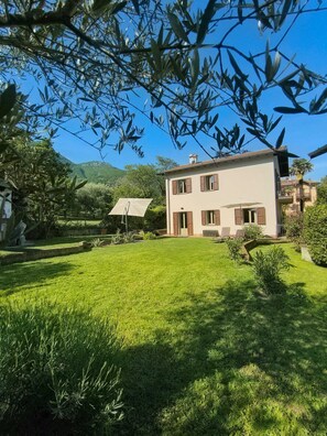 Une maison à deux étages avec une pelouse bien entretenue, une terrasse avec des chaises et une vue sur les montagnes en toile de fond.