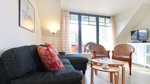 A living room with a sofa, two chairs, a small table, a lamp, a TV, and a window with curtains.