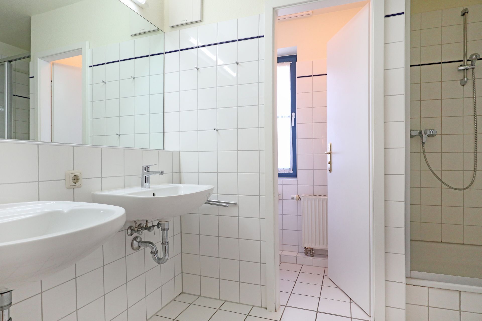 A bathroom with two sinks, a mirror, and a shower area.