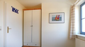 Ein Schlafzimmer mit Kleiderschrank, Bett, einem Fenster mit Vorhängen und einem gerahmten Bild an der Wand.