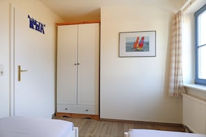 Une chambre avec une armoire, un lit, une fenêtre avec des rideaux et un tableau encadré au mur.