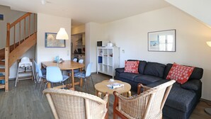 Een woonkamer met een bank, stoelen, een eettafel en een trap.