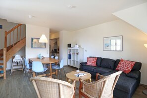 Ein Wohnzimmer mit einer Couch, Sesseln, einem Esstisch und einer Treppe.