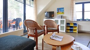 A room with two wicker chairs, a round wooden table, a television, and a painting on the wall.