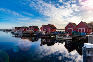 Une scène de bord de mer avec des bâtiments rouges, des bateaux et une eau calme qui reflète les structures environnantes.