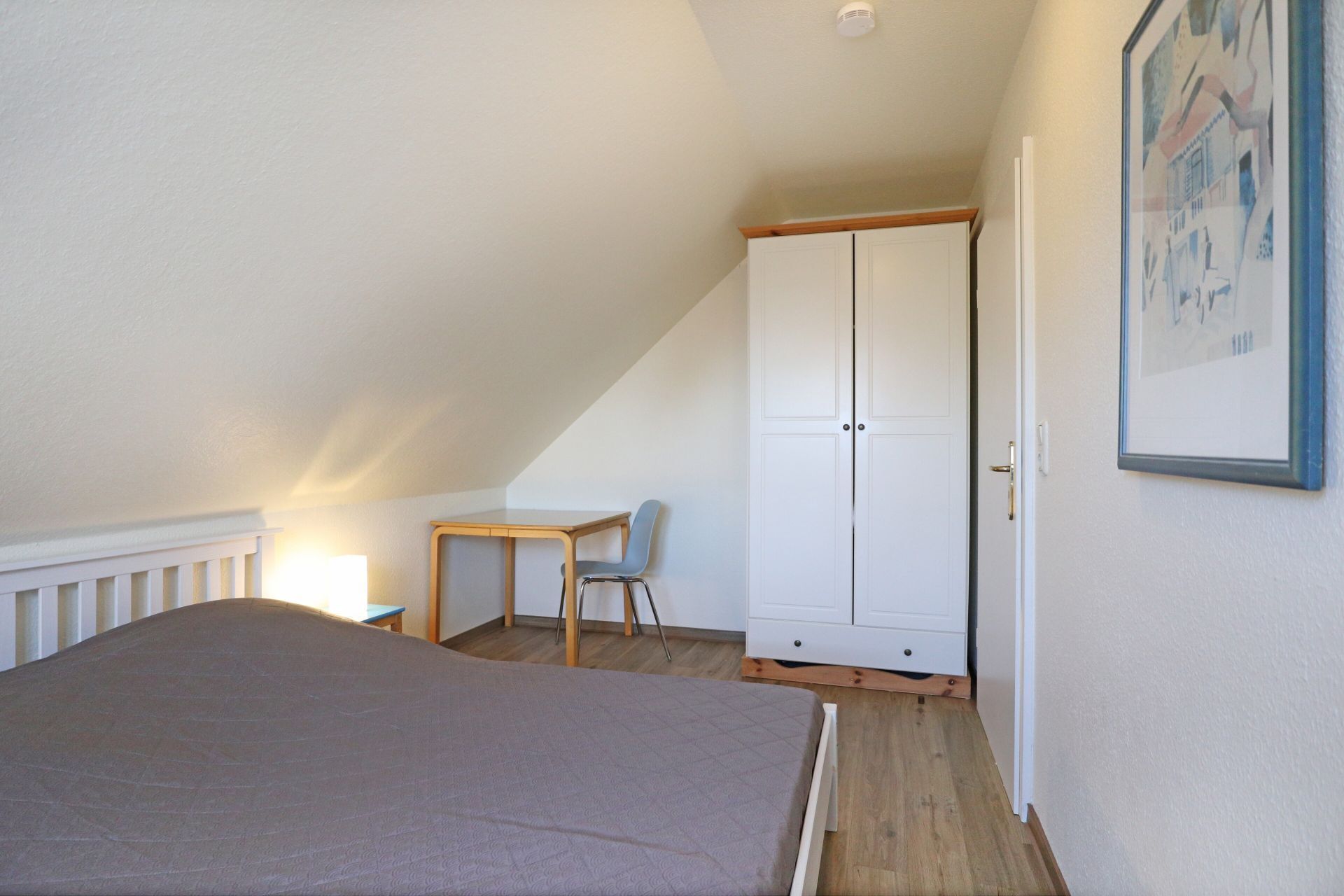 Un dormitorio con cama, escritorio, silla y armario.