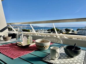 Un balcón con una mesa dispuesta para una comida, con vista a un puerto deportivo y al mar.
