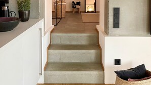 Un escalier moderne mène à un espace de vie au design minimaliste, agrémenté d’un grand miroir et d’un coin salon confortable.