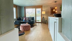Un salon moderne avec un canapé, un pouf et un coin repas agrémenté d’une lampe.
