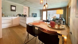 Une cuisine moderne avec des meubles blancs, une table à manger avec des chaises et des luminaires suspendus.