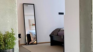 Une chambre d’hôtel moderne avec un grand miroir, un lit, une plante en pot et un bol posé sur une table.