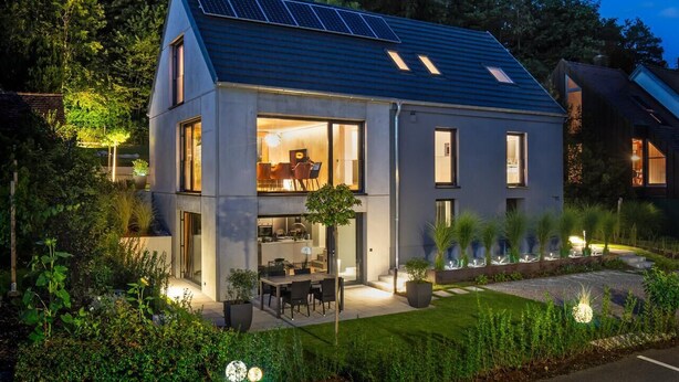 Une maison moderne dotée d’un toit en pente, de panneaux solaires et d’un intérieur bien éclairé.