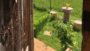 Puerta de madera rústica con un adorno en forma de corazón y vista a un campo verde exuberante, con una pequeña mesa y un jarrón de flores.