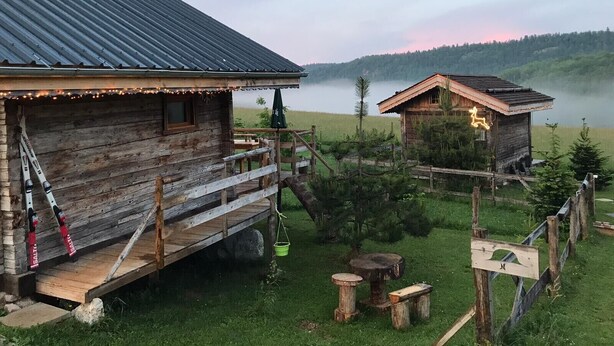 Una cabaña rústica con techo de metal, una terraza de madera y un pequeño porche.
