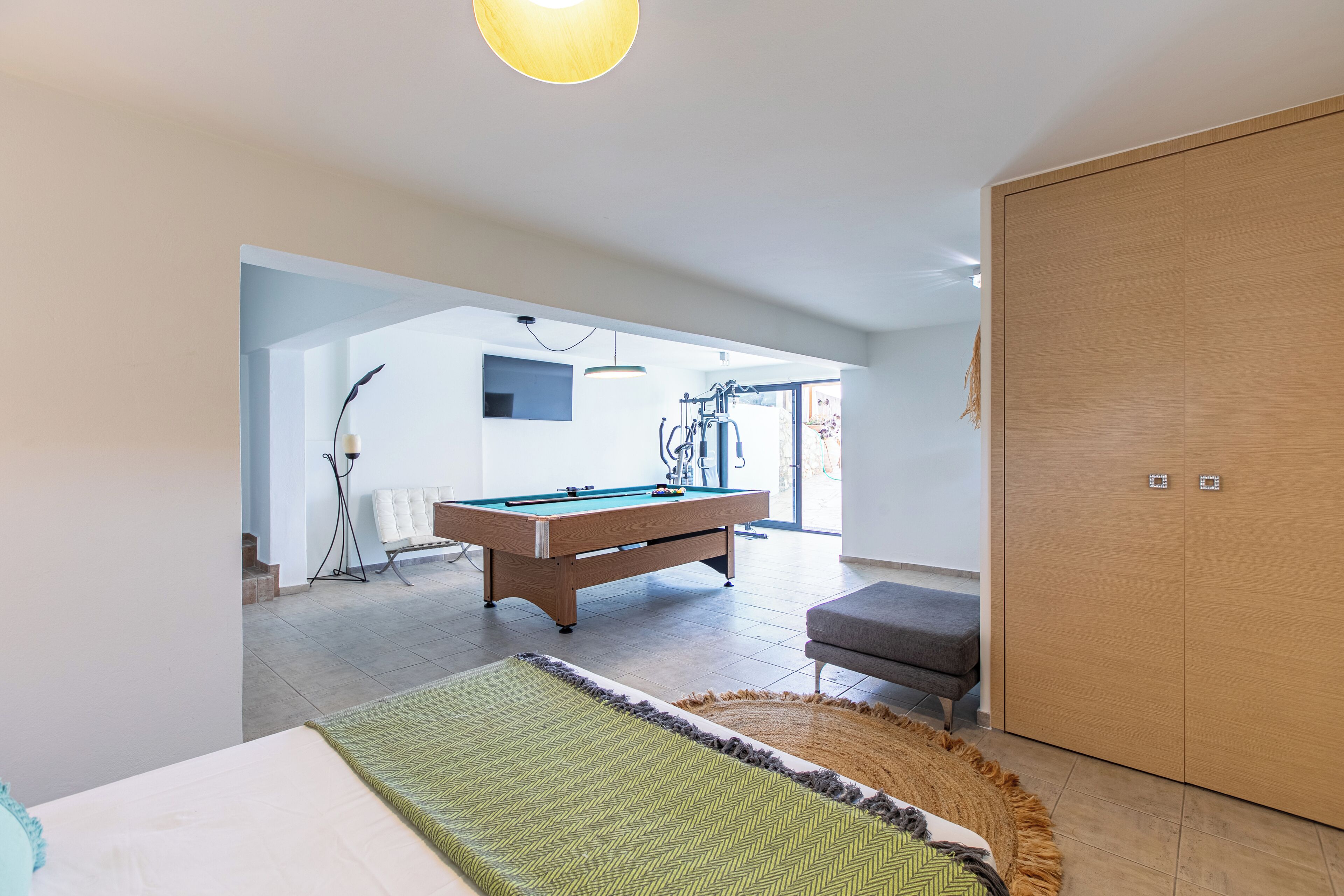 A modern living room with a pool table, a sofa, and a large wooden wardrobe.