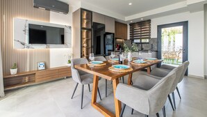 A modern kitchen with a built-in oven, a large flat-screen TV, and a dining area with a wooden table and grey chairs. - 300mt to Restaurants & Supermarkets *1km to Beach*Gym (Plaka)