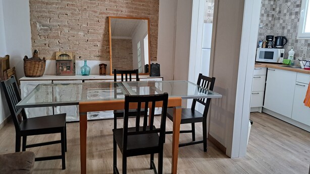 A dining area with a glass table, black chairs, a brick wall, and a kitchen in the background. - Casa Antique Barcelona&Barca (Hospitalet de Llobregat)