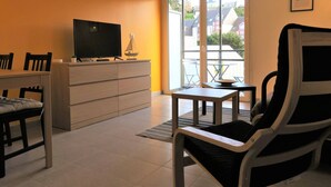 A living room with a TV on a dresser, a dining table with chairs, and a view through a glass door to the outside. - New apartment 2/4 people, 100m to beach, Perros-Guirec (Perros-Guirec)