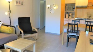 A modern living room with a sofa, a black armchair, a small table, and a dining area with chairs and a wooden table. - New apartment 2/4 people, 100m to beach, Perros-Guirec (Perros-Guirec)