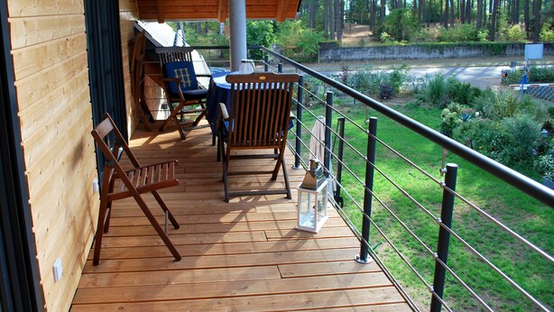 A wooden deck with outdoor furniture, a lantern, and a view of a forested area. - Apartment "SeeLiebe" in Bad Saarow (Bad Saarow)