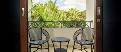 A balcony with three wicker chairs and a small table, overlooking lush greenery and a clear sky.