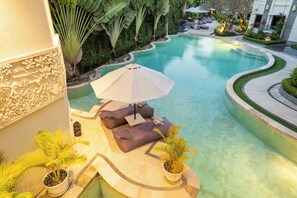A curved pool with a seating area featuring a beige umbrella and cushions. - Bali Karma Sajtra Hotel (Keroboken Kelod)