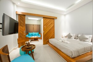 Quarto de hotel moderno com cama, televisão, sofá e uma mesinha.