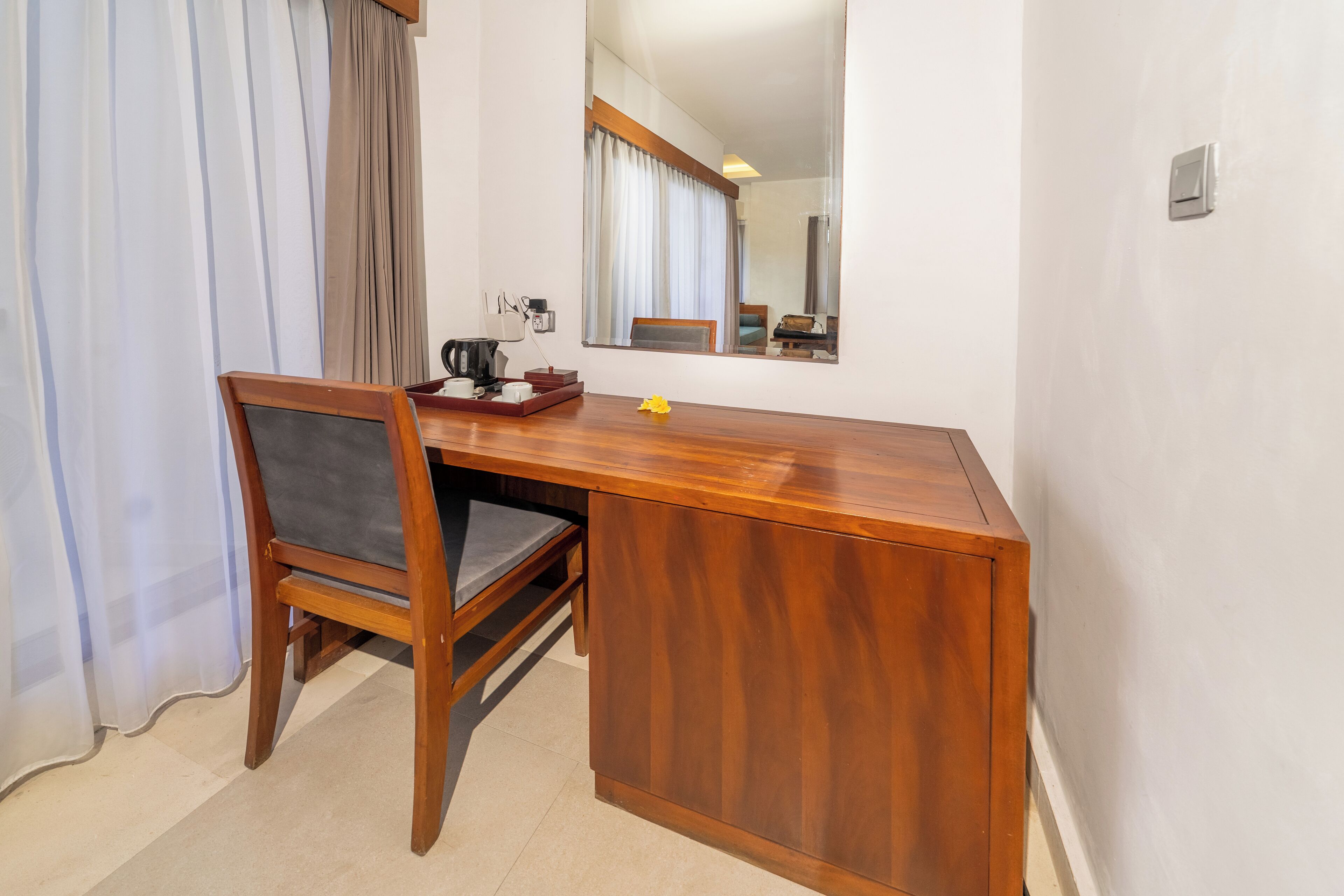 A wooden desk with a chair, a mirror, and a small table with a kettle and cups.