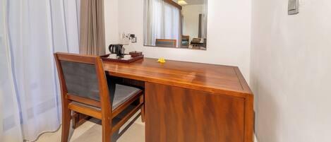 A wooden desk with a chair, a mirror, and a small table with a kettle and cups.