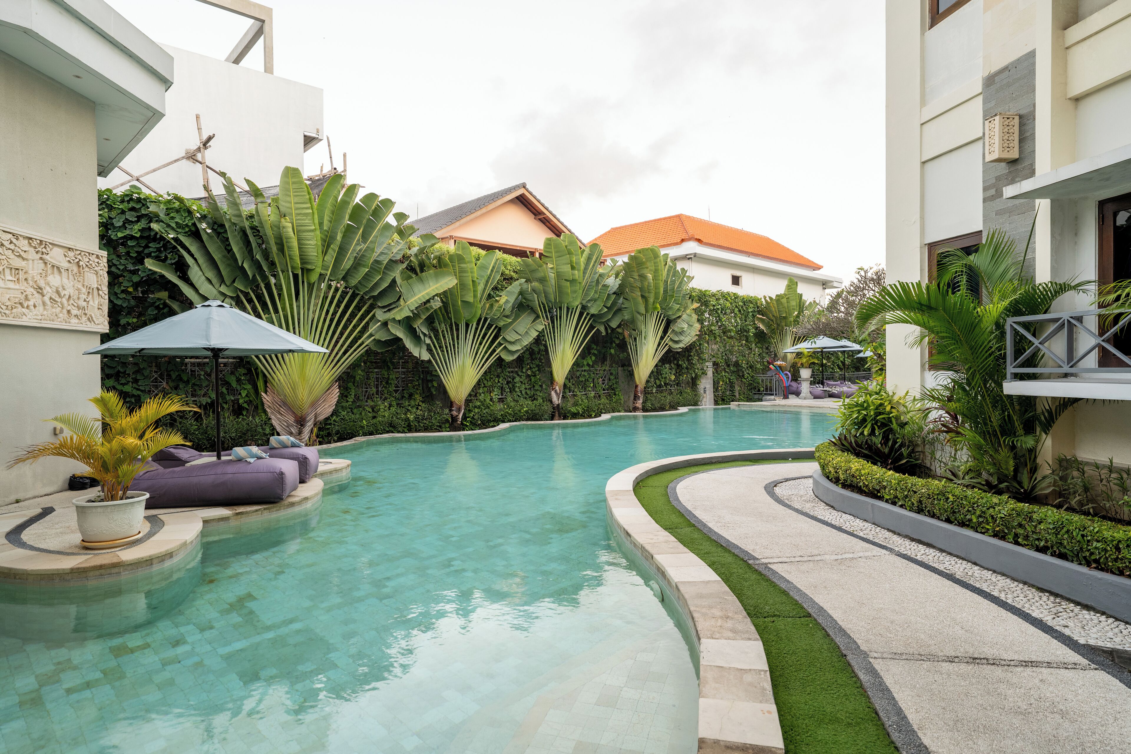 Ein Pool mit geschwungener Kante, umgeben von üppiger Bepflanzung und einigen Liegestühlen.