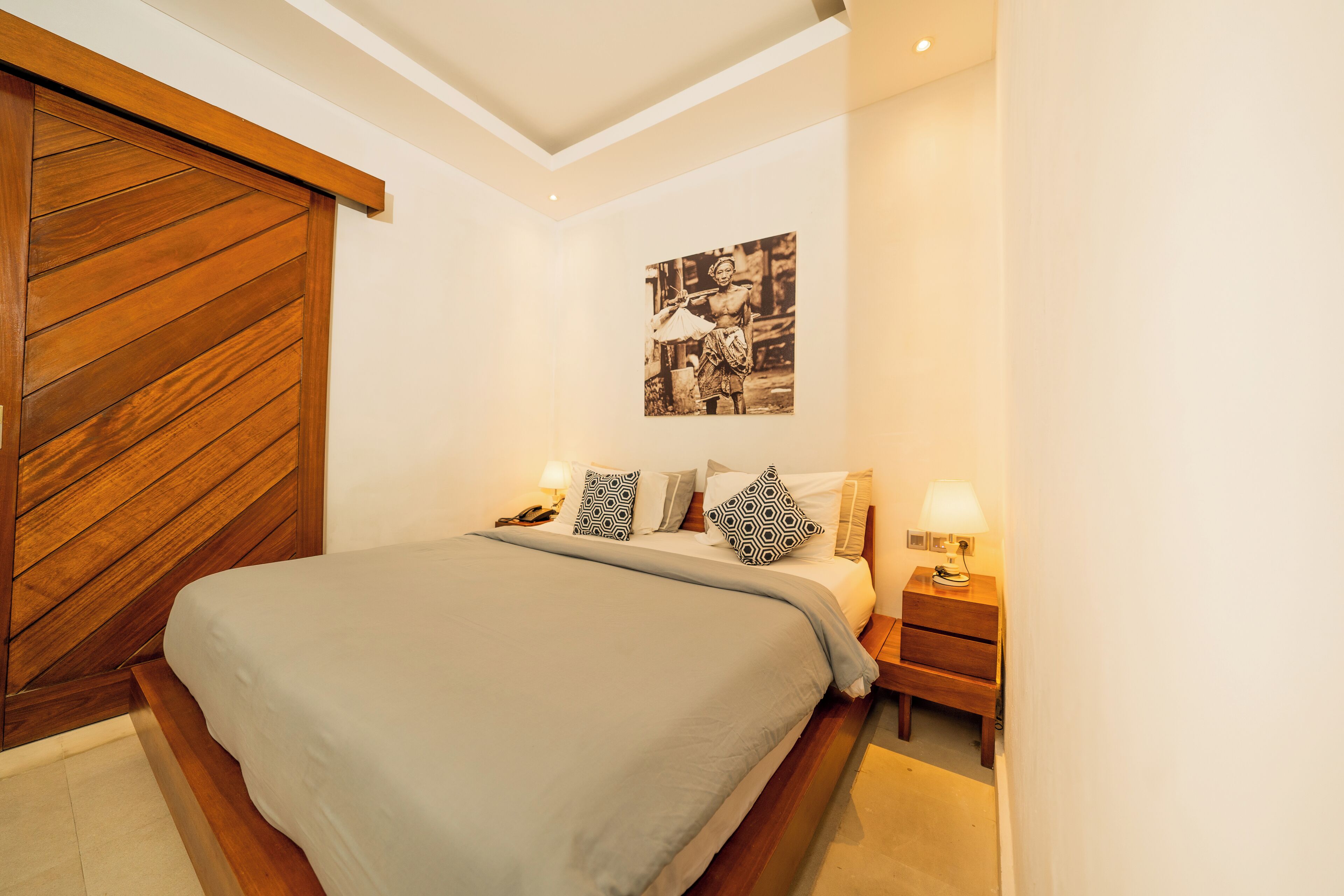 Un dormitorio con una cama grande, cabecera de madera, mesitas de noche con lámparas y un cuadro en la pared.