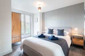 Et moderne hotelværelse med en stor seng, et træskab, en grå sengegavl og et natbord med en lampe.