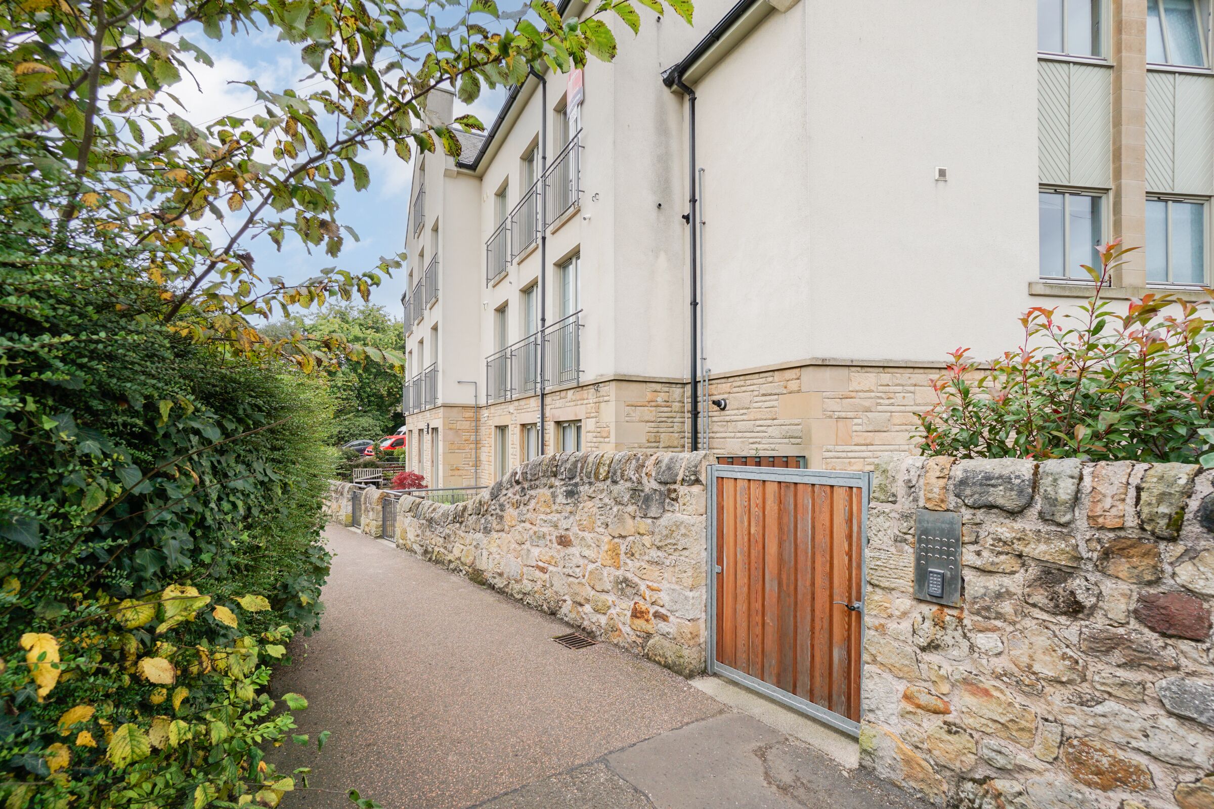 Un étroit sentier mène à un bâtiment aux murs de pierre, doté d’une porte en bois et d’un système de verrouillage à clavier.