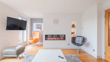 Ein modernes Wohnzimmer mit Fernseher, Kamin und zwei Sesseln.