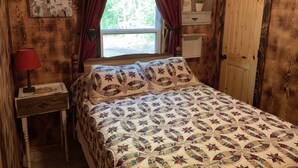 Um quarto acolhedor com parede de madeira, cama com colcha, mesa de cabeceira com abajur e janela com cortinas.