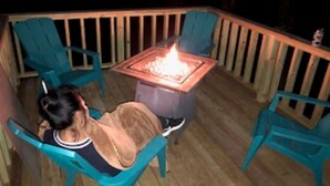 Pessoa relaxando em uma cadeira ao lado de um deck de madeira com lareira.