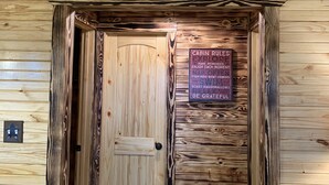 Entrada de uma cabana de madeira, com decoração de cabeça de veado, uma placa com regras da cabana e um adorno em formato de estrela no chão.