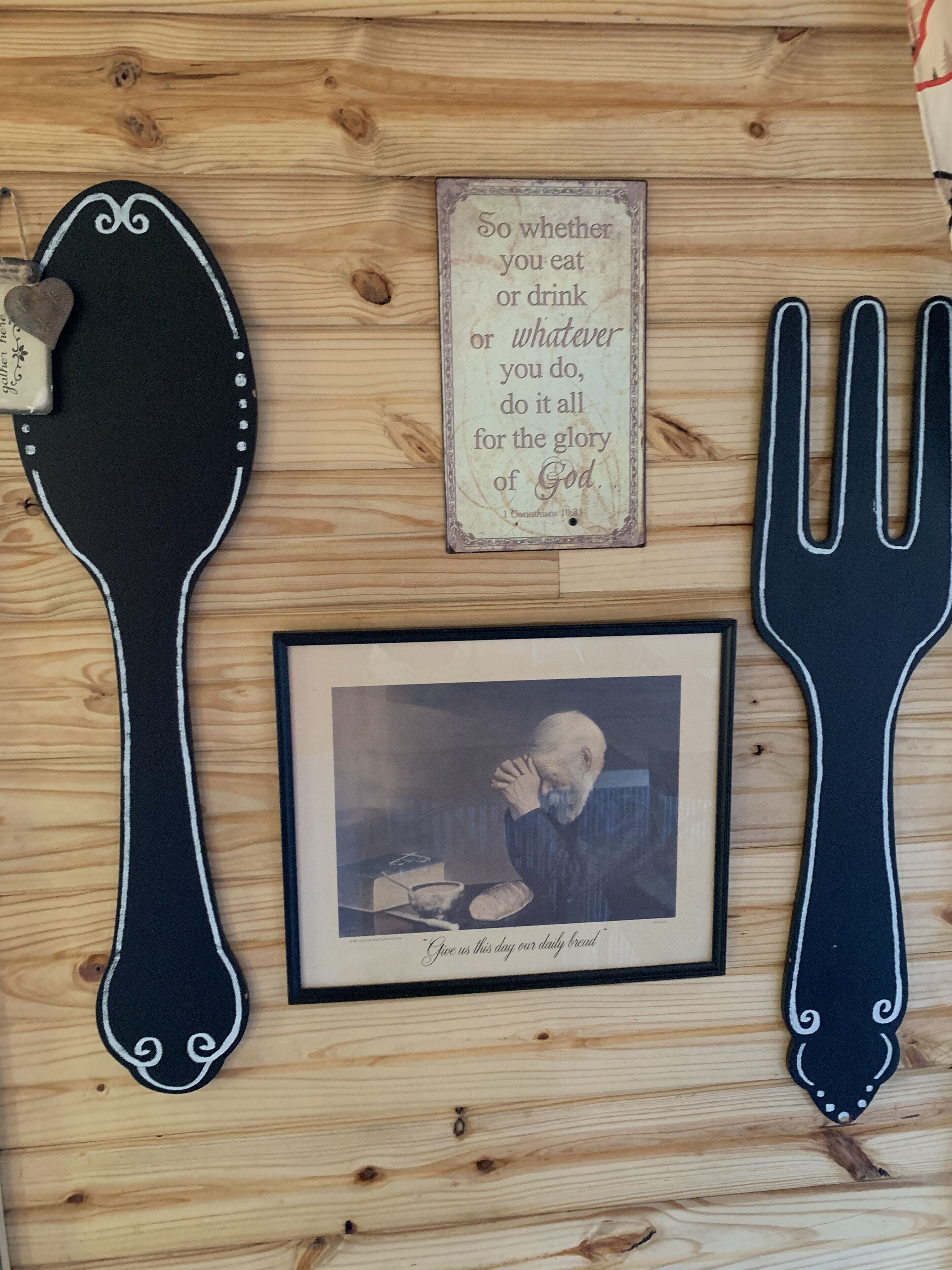 A wooden wall with a framed inspirational quote, a framed photograph, and two black utensils.