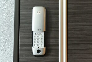 Un système d’interphone moderne, argenté, fixé au mur, doté d’un clavier numérique et d’une grille de haut-parleur, installé sur une porte en bois foncé.