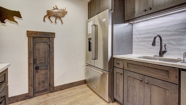 A kitchen with wooden cabinets, a stainless steel refrigerator, a sink with a modern faucet, and decorative wall art. - Motherlode C9 2 Bedroom Condo by RedAwning (Breckenridge)